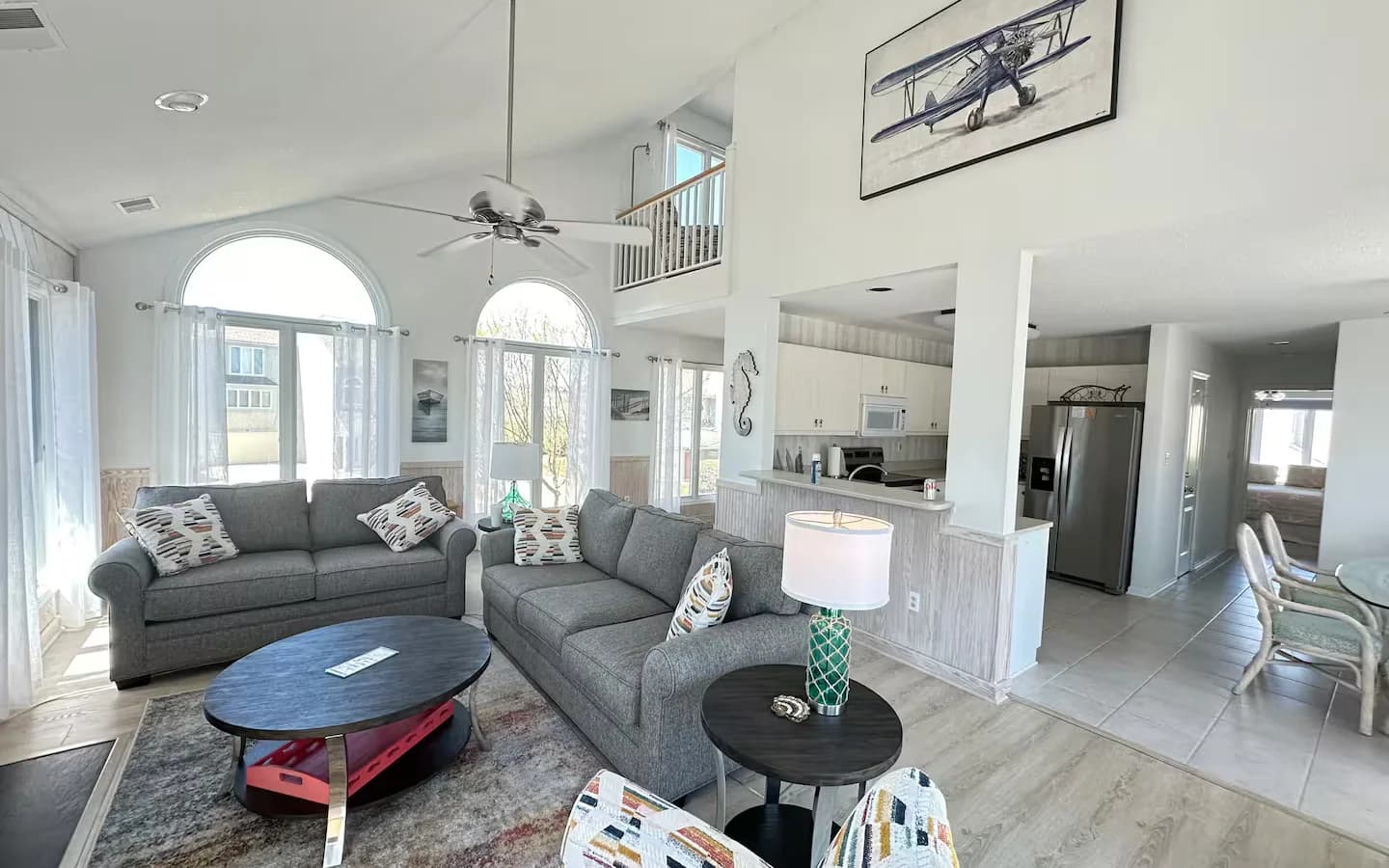 Shore Nuff living room — open-plan space with vaulted ceiling, grey sofas, and natural light through large arched windows